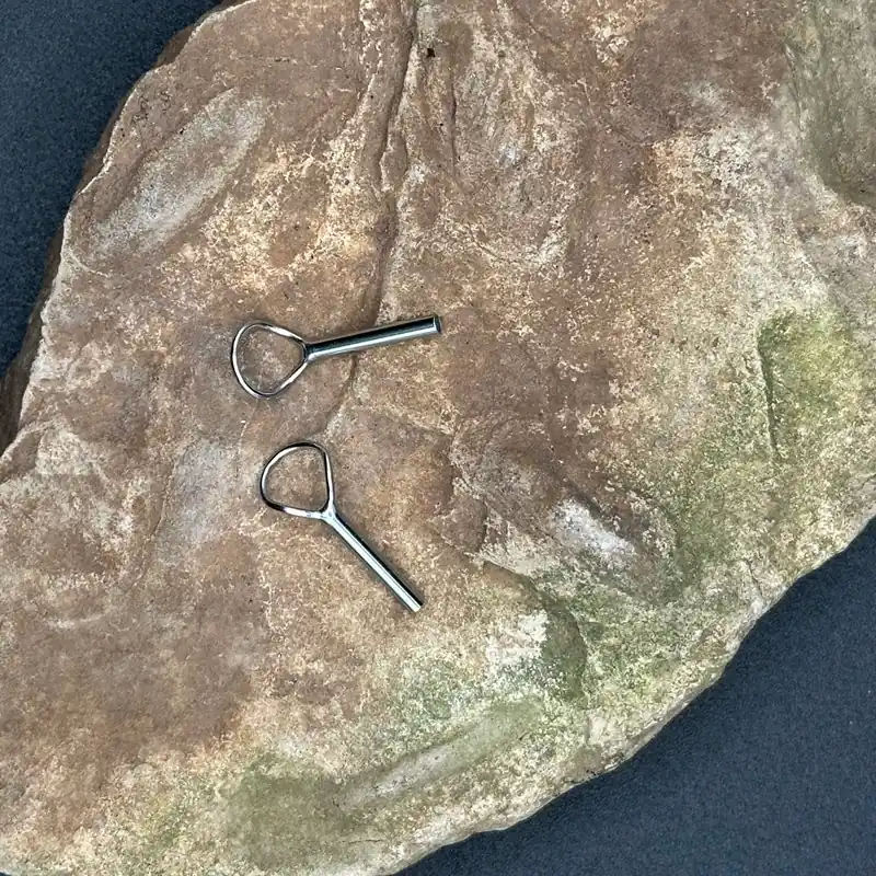 Pac Bay XFTL tip top guides for fly rods in super hard chrome, showing two sizes — one with a tube base and one with a flat worm-style base, displayed on a natural stone surface.