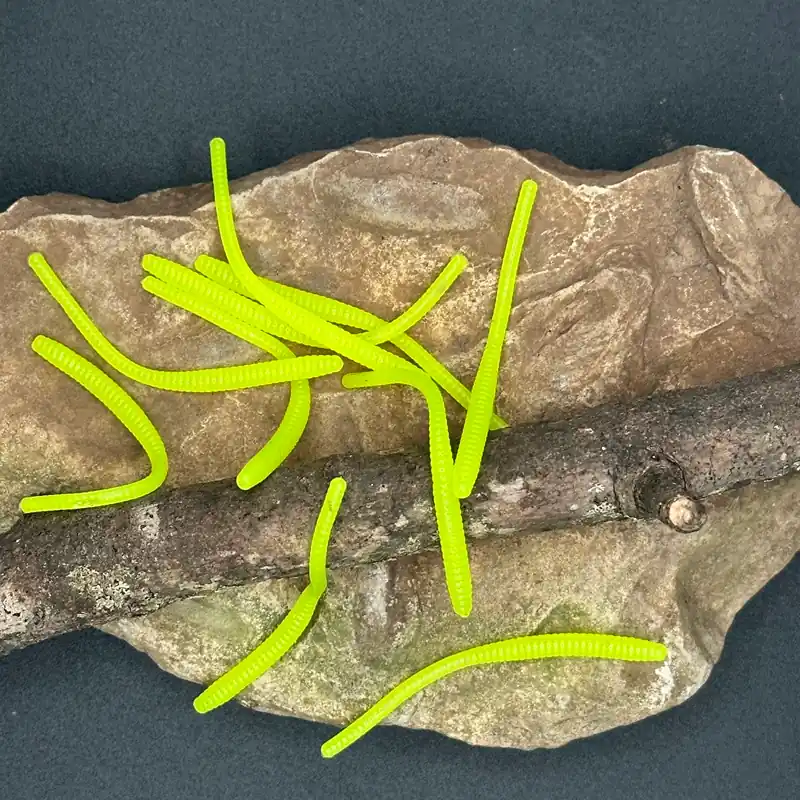 Family Fishin hand-injected soft plastic trout worms in chartreuse — ribbed bright yellow-green body displayed on natural Ozarks stone and driftwood.