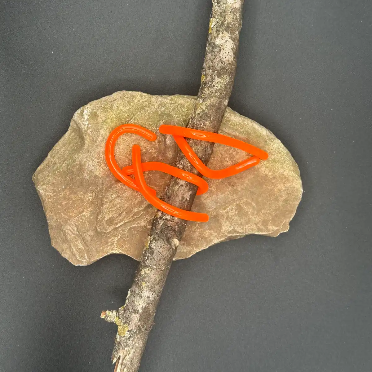 Orange 2.95 inch round worm soft plastic bait by Family Fishin on rock and driftwood